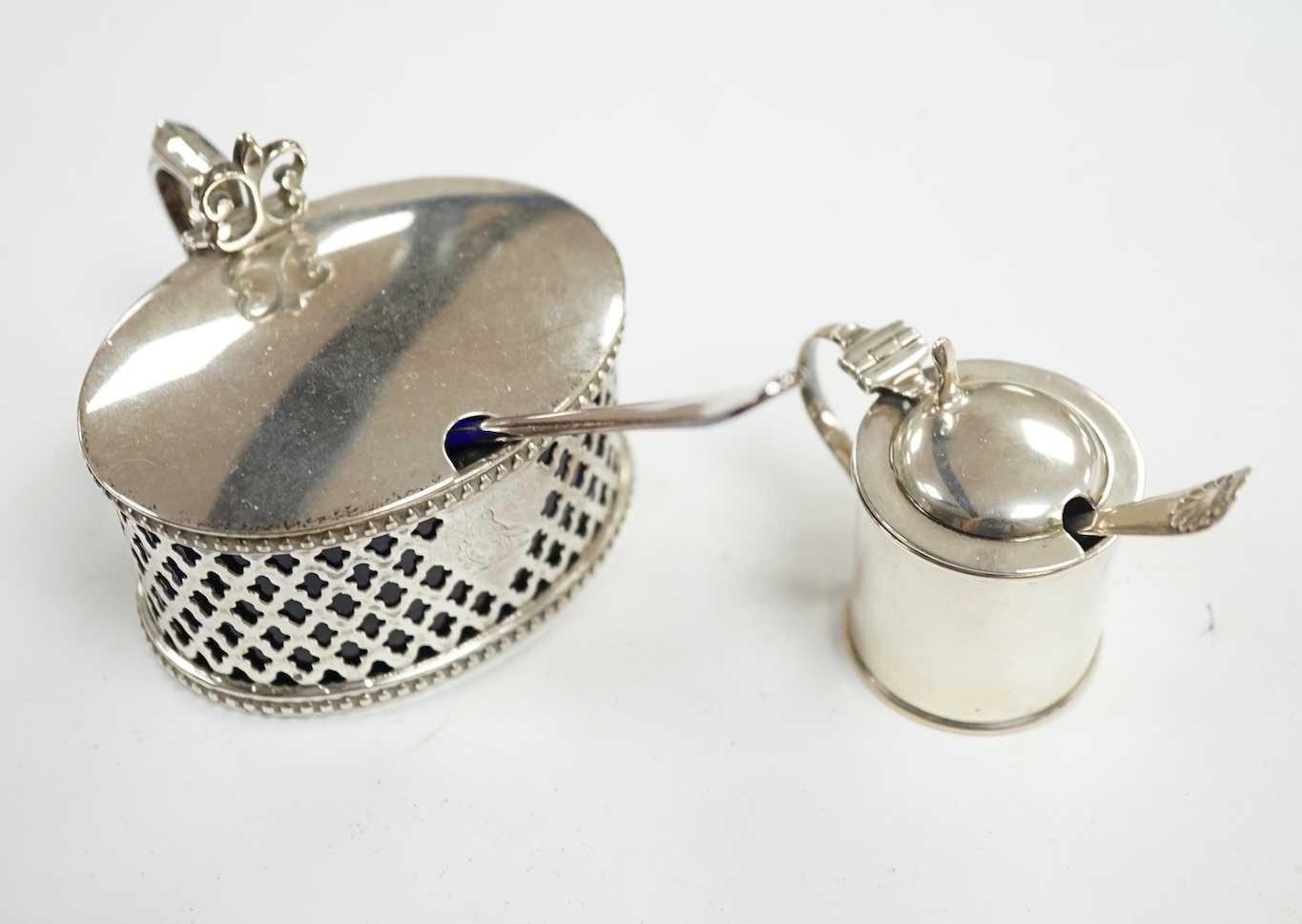 A Victorian pierced silver oval mustard pot by Henry Wilkinson & Co Ltd, Sheffield, 1851, 84mm, with blue glass liner and associated plated spoon, together with a smaller later silver mustard pot. Condition - fair